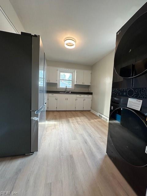 kitchen with stainless steel refrigerator, white cabinetry, sink, stacked washer / drying machine, and light wood-type flooring