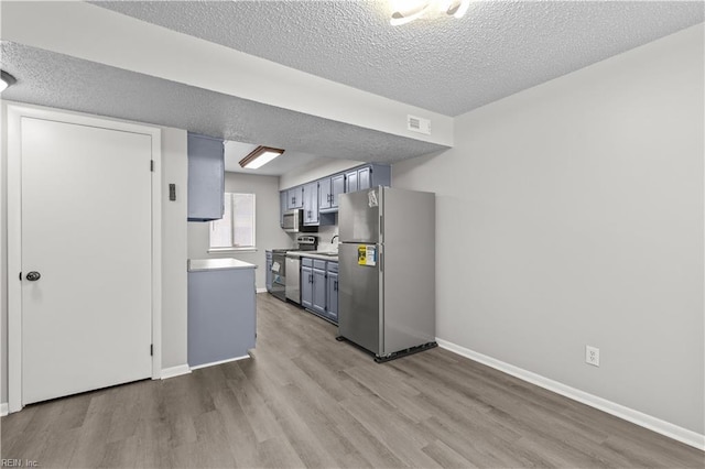 kitchen with appliances with stainless steel finishes, a textured ceiling, and light hardwood / wood-style flooring