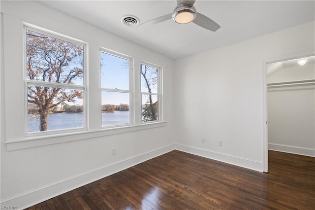 unfurnished bedroom featuring ceiling fan, a closet, a water view, and dark wood-type flooring