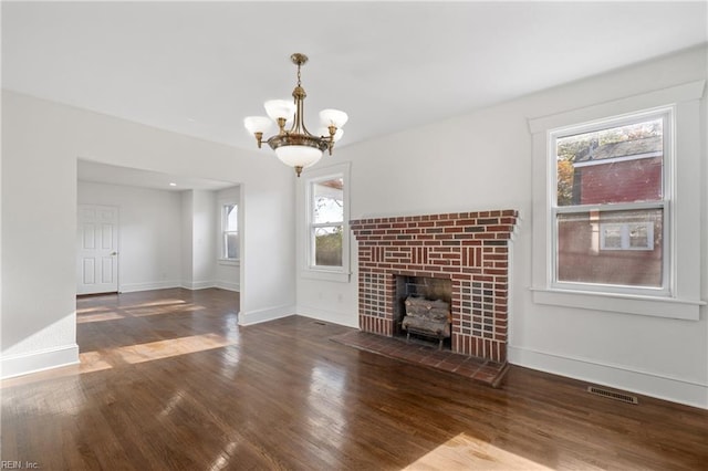 unfurnished living room featuring a fireplace, dark hardwood / wood-style floors, an inviting chandelier, and a healthy amount of sunlight