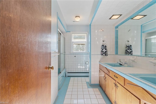 bathroom featuring baseboard heating, tile patterned flooring, combined bath / shower with glass door, vanity, and tile walls