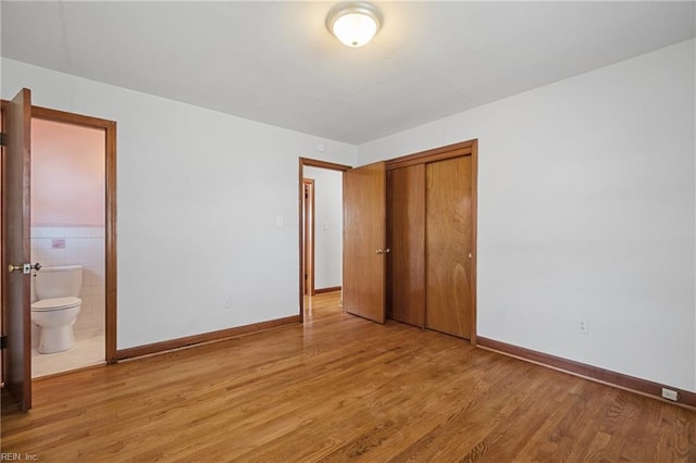 unfurnished bedroom with ensuite bathroom, a closet, tile walls, and light hardwood / wood-style flooring