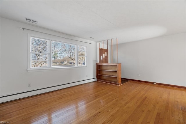 empty room featuring hardwood / wood-style flooring and a baseboard heating unit