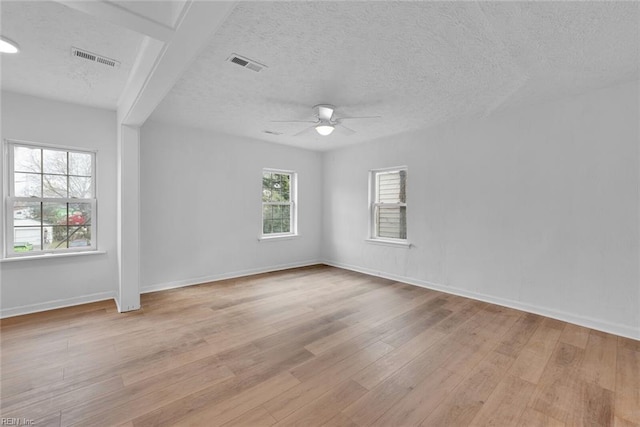 empty room featuring a textured ceiling, a wealth of natural light, and light hardwood / wood-style flooring