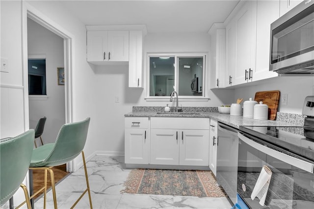 kitchen featuring light stone counters, stainless steel appliances, white cabinetry, and sink