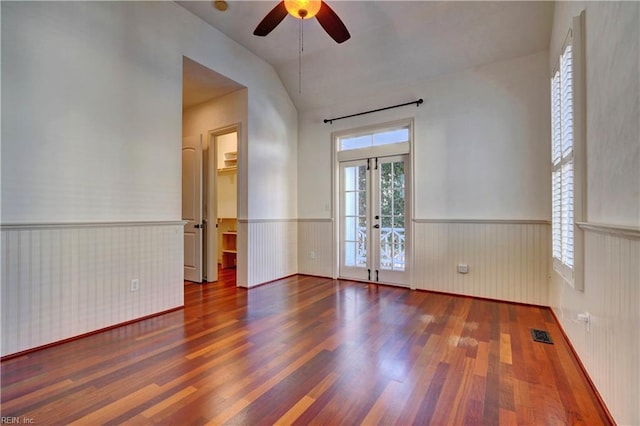 empty room featuring wooden walls, vaulted ceiling, ceiling fan, and dark wood-type flooring