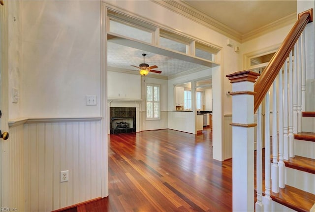 interior space with ceiling fan, wood-type flooring, crown molding, and a tiled fireplace