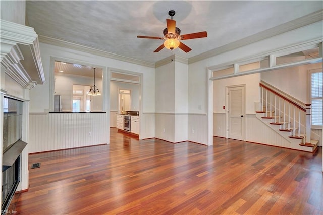 unfurnished living room featuring wood-type flooring, ceiling fan with notable chandelier, and ornamental molding