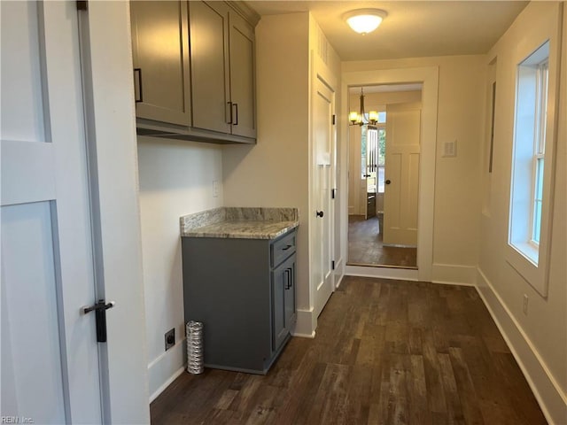 kitchen with light stone countertops, gray cabinets, dark wood-type flooring, and a notable chandelier