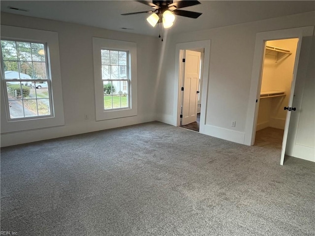 unfurnished bedroom with dark colored carpet, a closet, a spacious closet, and multiple windows