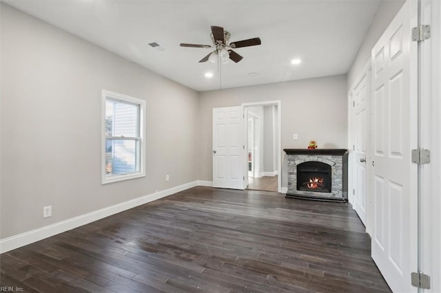 unfurnished living room with ceiling fan, dark hardwood / wood-style floors, and a stone fireplace