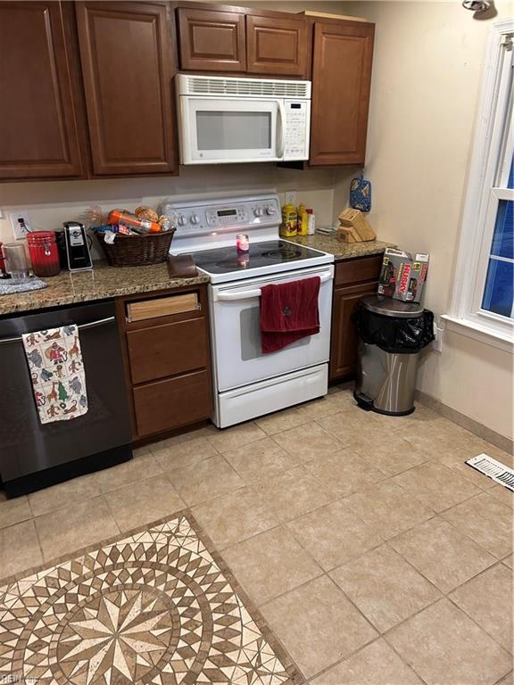 kitchen with light tile patterned floors, dark stone counters, and white appliances