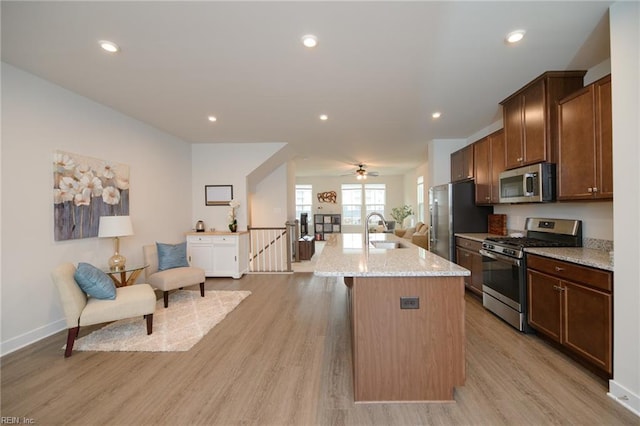 kitchen with sink, an island with sink, appliances with stainless steel finishes, light hardwood / wood-style floors, and light stone counters