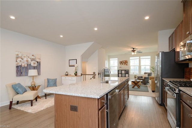 kitchen featuring appliances with stainless steel finishes, light wood-type flooring, ceiling fan, a kitchen island with sink, and sink