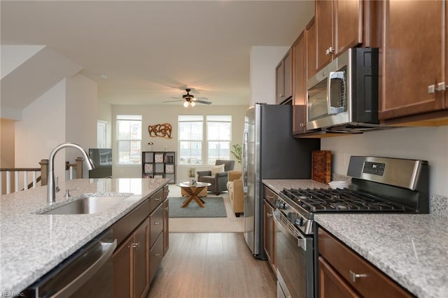 kitchen with light stone countertops, light wood-type flooring, stainless steel appliances, ceiling fan, and sink