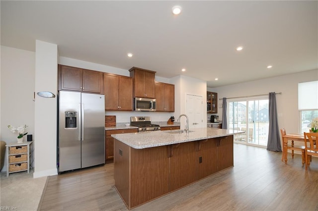 kitchen featuring sink, a kitchen island with sink, a breakfast bar, appliances with stainless steel finishes, and light wood-type flooring