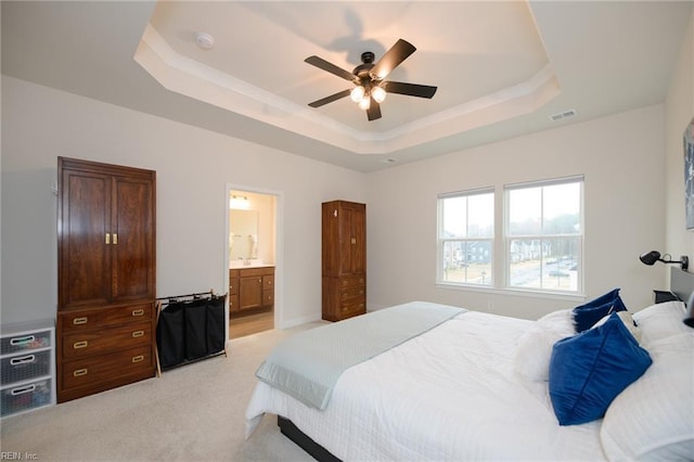 carpeted bedroom with a tray ceiling, connected bathroom, and ceiling fan