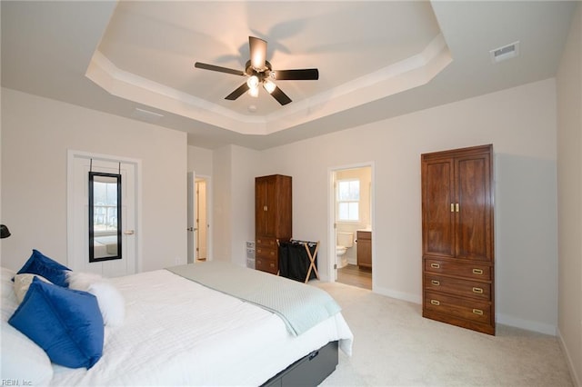 bedroom with ceiling fan, a raised ceiling, light carpet, and connected bathroom