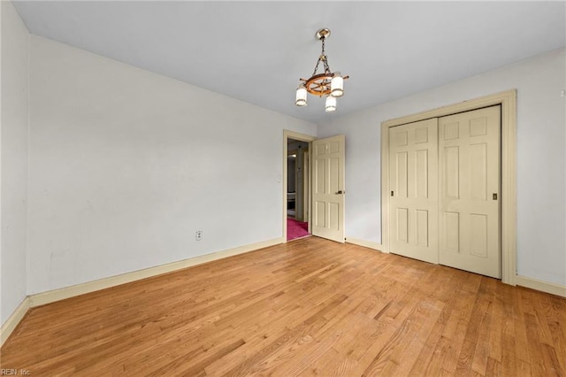 unfurnished bedroom featuring a closet, light hardwood / wood-style floors, and a notable chandelier