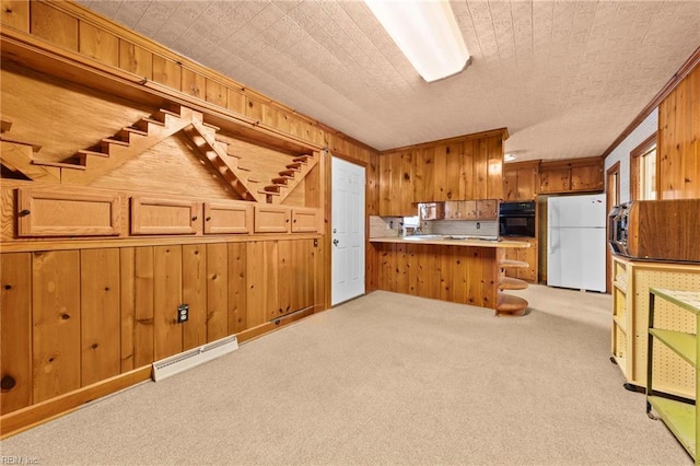 kitchen with kitchen peninsula, light carpet, wooden walls, white fridge, and oven