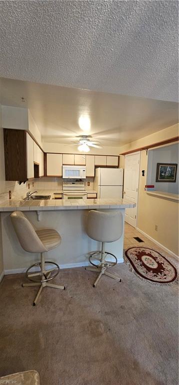 kitchen with a breakfast bar area, kitchen peninsula, white cabinets, and white appliances