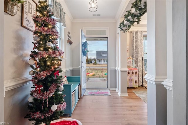 doorway to outside with decorative columns, ornamental molding, a wealth of natural light, and light hardwood / wood-style flooring