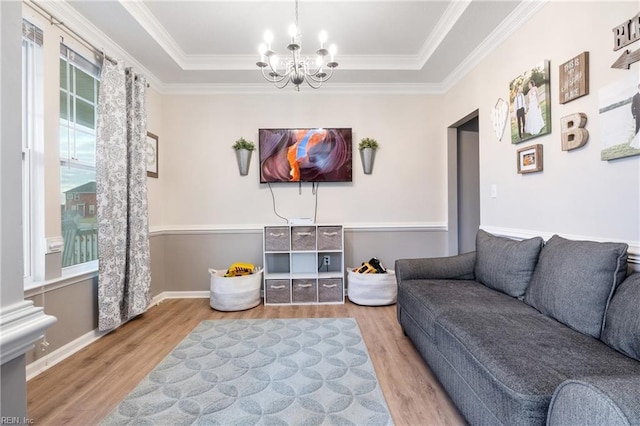 living room featuring hardwood / wood-style floors, ornamental molding, a tray ceiling, and a chandelier