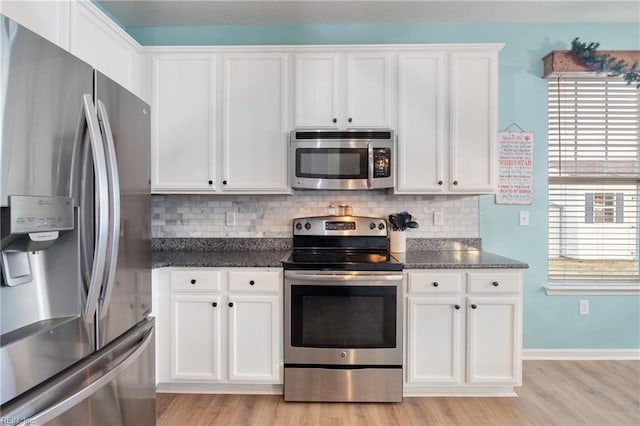 kitchen with dark stone countertops, white cabinetry, light wood-type flooring, and appliances with stainless steel finishes