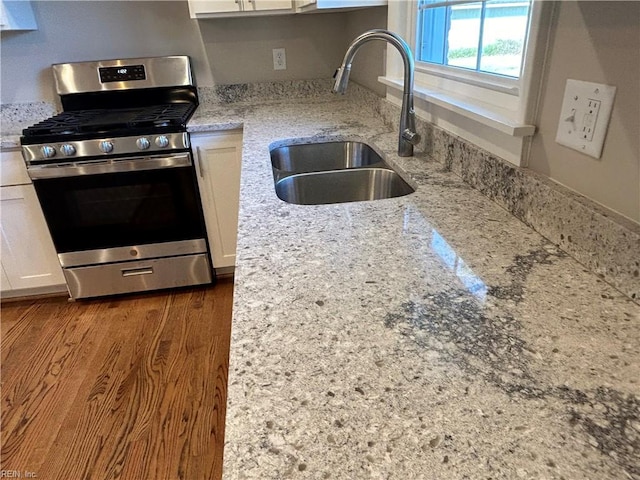 kitchen featuring light stone countertops, dark hardwood / wood-style flooring, sink, white cabinets, and stainless steel gas stove