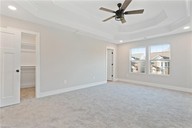 unfurnished bedroom with a spacious closet, ceiling fan, a tray ceiling, light carpet, and a closet