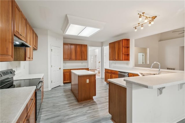 kitchen featuring sink, light wood-type flooring, appliances with stainless steel finishes, a kitchen island, and kitchen peninsula