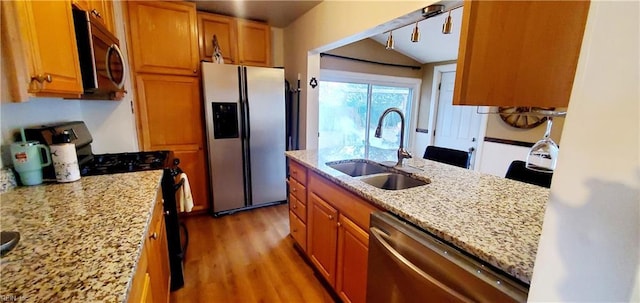 kitchen featuring appliances with stainless steel finishes, light stone counters, vaulted ceiling, sink, and light hardwood / wood-style floors