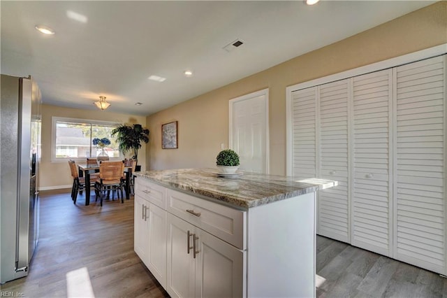 kitchen featuring white cabinetry, light stone countertops, stainless steel fridge with ice dispenser, a kitchen island, and light wood-type flooring