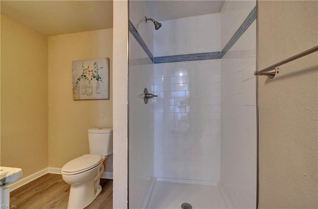 bathroom with a tile shower, hardwood / wood-style floors, and toilet