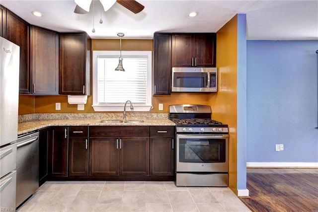 kitchen featuring appliances with stainless steel finishes, light wood-type flooring, light stone counters, dark brown cabinetry, and sink