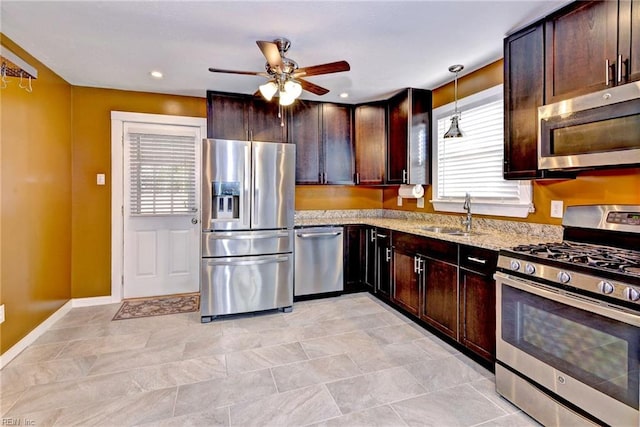 kitchen featuring ceiling fan, sink, hanging light fixtures, stainless steel appliances, and light stone counters