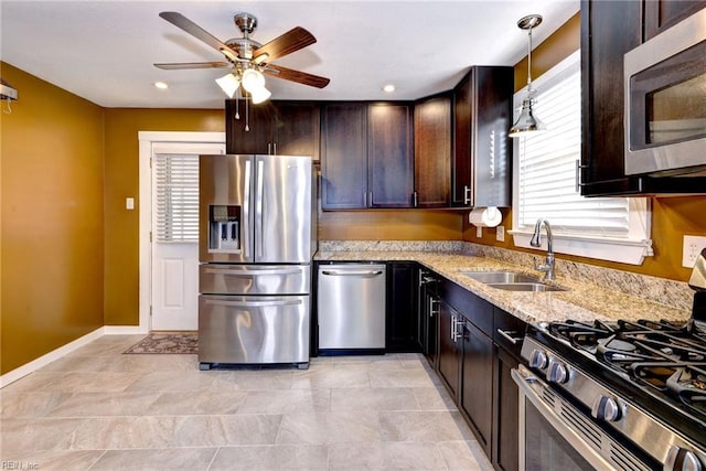 kitchen featuring sink, appliances with stainless steel finishes, decorative light fixtures, light stone counters, and dark brown cabinetry