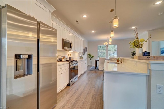 kitchen with white cabinetry, sink, hanging light fixtures, stainless steel appliances, and light hardwood / wood-style floors