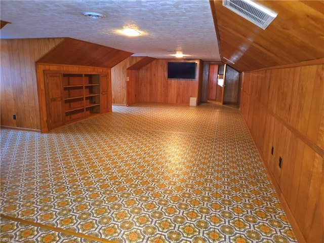 bonus room with lofted ceiling, built in shelves, wooden walls, and a textured ceiling