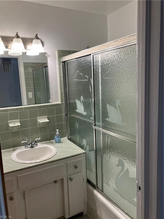 bathroom with tasteful backsplash, vanity, bath / shower combo with glass door, and tile walls