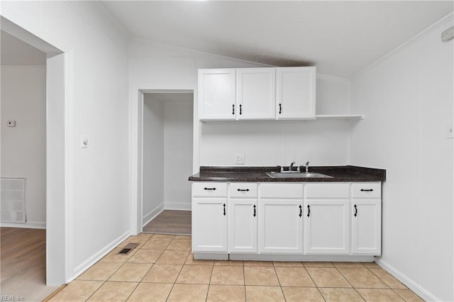 kitchen with white cabinetry, sink, light tile patterned floors, and vaulted ceiling