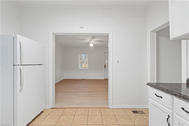 kitchen with white cabinetry, ceiling fan, white fridge, dark stone counters, and light hardwood / wood-style floors