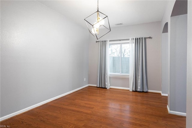 spare room with a notable chandelier and dark hardwood / wood-style floors