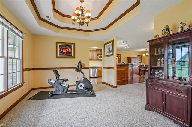 exercise room featuring a tray ceiling, light carpet, ornamental molding, and a notable chandelier