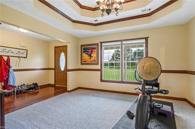 workout room featuring a chandelier, hardwood / wood-style floors, a tray ceiling, and ornamental molding