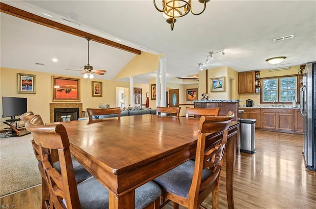 dining room with ornate columns, sink, lofted ceiling with beams, wood-type flooring, and ceiling fan with notable chandelier