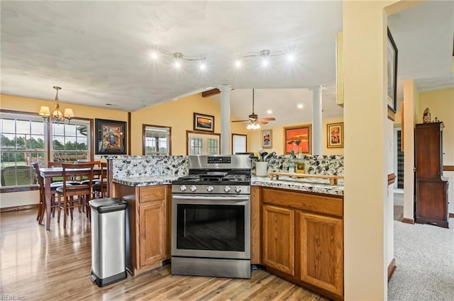 kitchen with kitchen peninsula, ceiling fan with notable chandelier, decorative light fixtures, light hardwood / wood-style flooring, and stainless steel range with gas cooktop