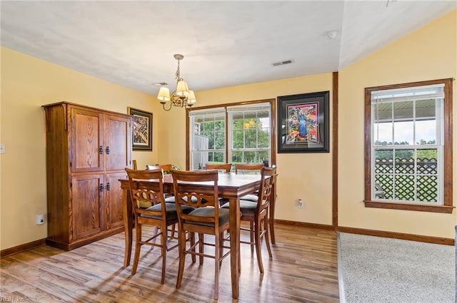 dining area with a notable chandelier, lofted ceiling, a wealth of natural light, and light hardwood / wood-style flooring