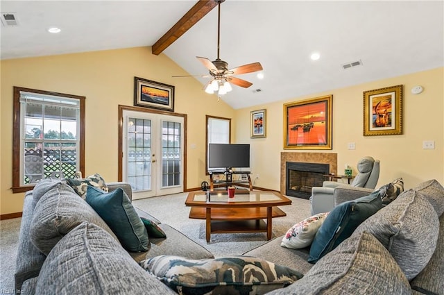 carpeted living room featuring french doors, vaulted ceiling with beams, ceiling fan, and a tiled fireplace