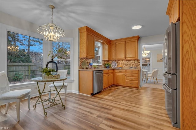 kitchen featuring stainless steel appliances, tasteful backsplash, a chandelier, pendant lighting, and light wood-type flooring